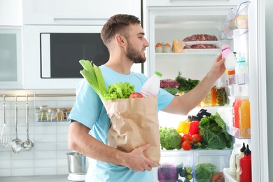 Man with paper bag putting products into refrigerator in kitchen