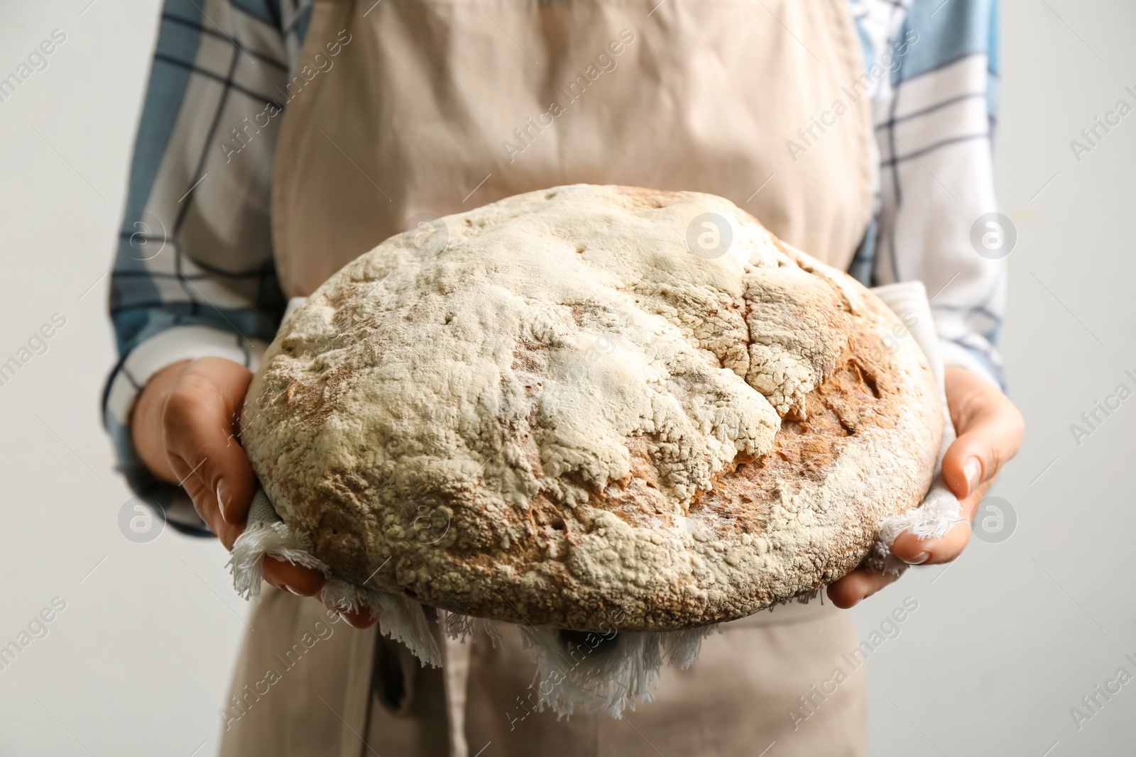 Photo of Woman holding freshly baked bread on grey background, closeup