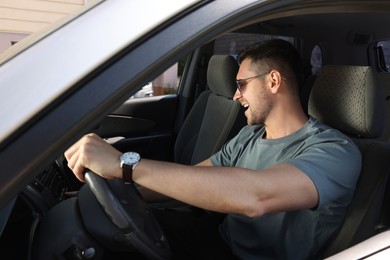 Photo of Listening to radio while driving. Handsome man with stylish sunglasses enjoying music in car