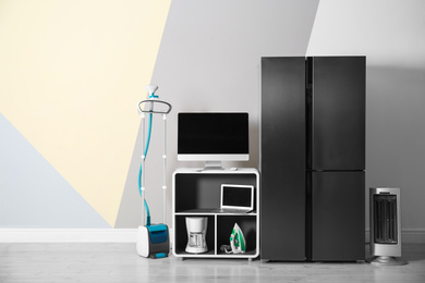 Photo of Modern refrigerator and other household appliances near color wall indoors