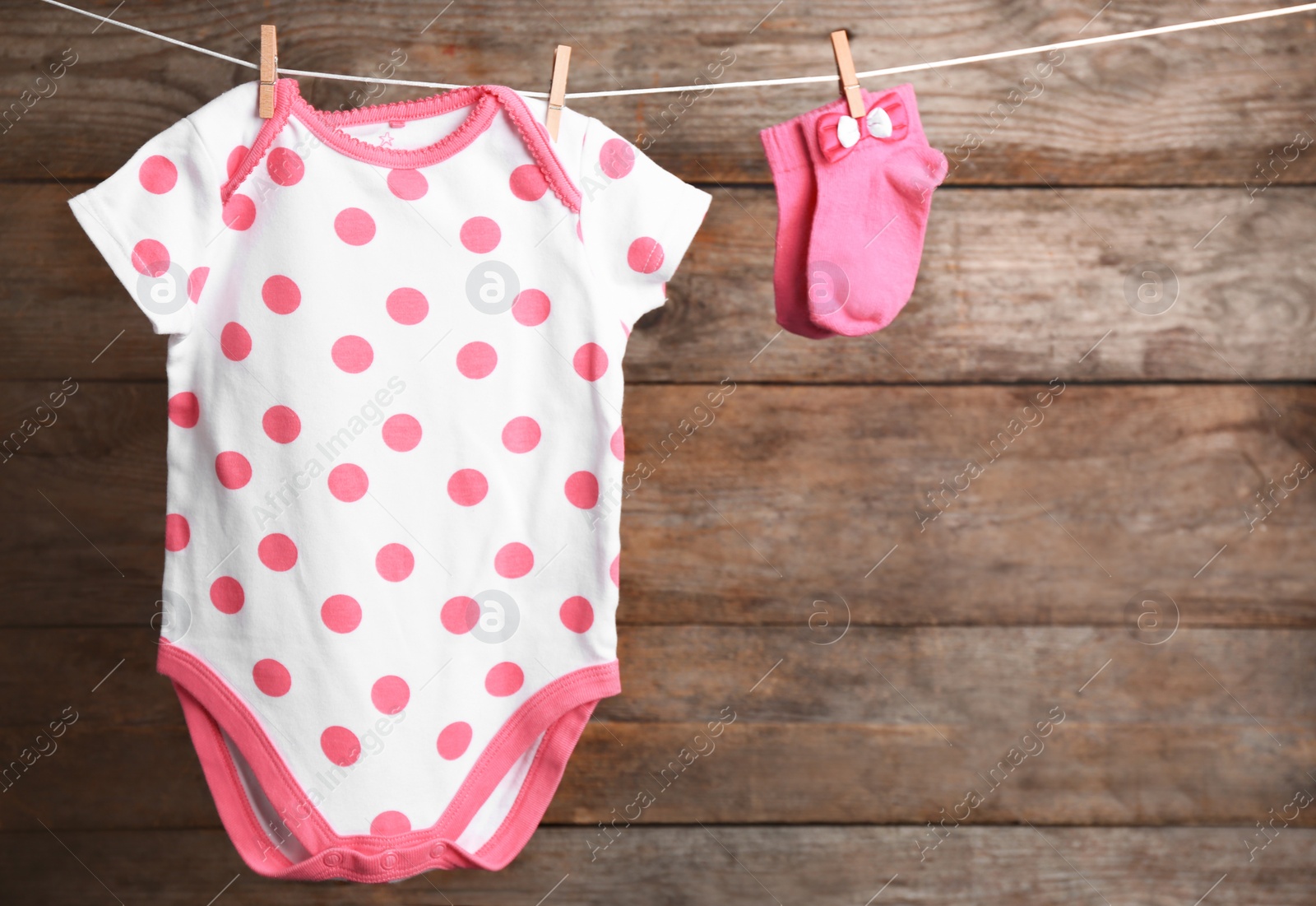 Photo of Bodysuit and socks on laundry line against wooden background, space for text. Baby accessories