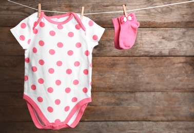 Photo of Bodysuit and socks on laundry line against wooden background, space for text. Baby accessories