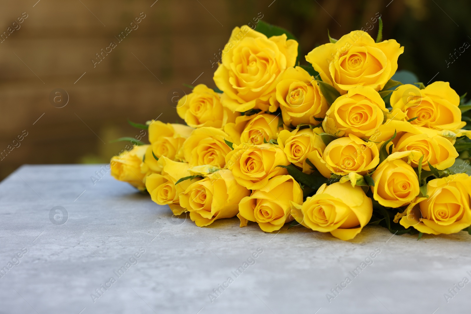 Photo of Beautiful bouquet of yellow roses on light table outdoors, space for text