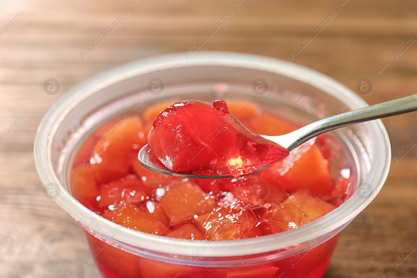 Photo of Spoon with fruit jelly over plastic container on table, closeup