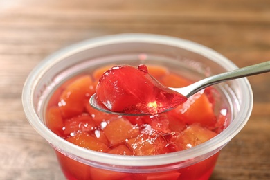 Photo of Spoon with fruit jelly over plastic container on table, closeup