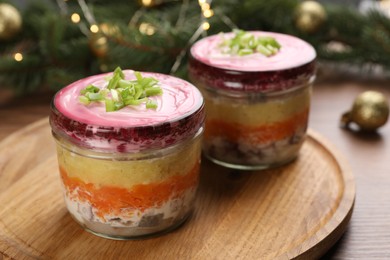 Glass jars with herring under fur coat and Christmas decor on wooden table. Traditional Russian salad