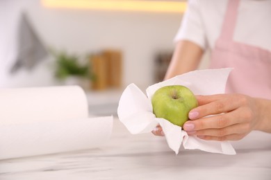 Photo of Woman wiping green apple with paper towel in kitchen, closeup