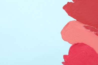 Smears of different beautiful lipsticks on light blue background, top view. Space for text