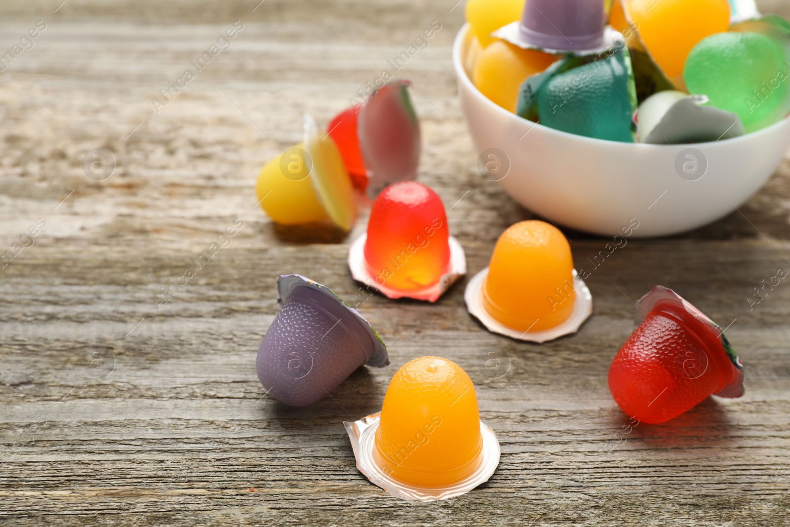 Photo of Bowl with tasty bright jelly cups on wooden table, space for text