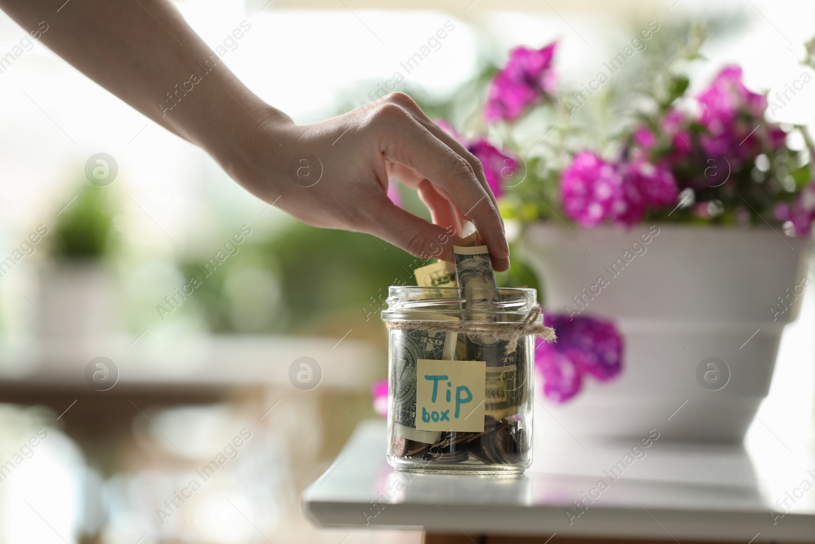 Photo of Woman putting tips into glass jar at table, closeup