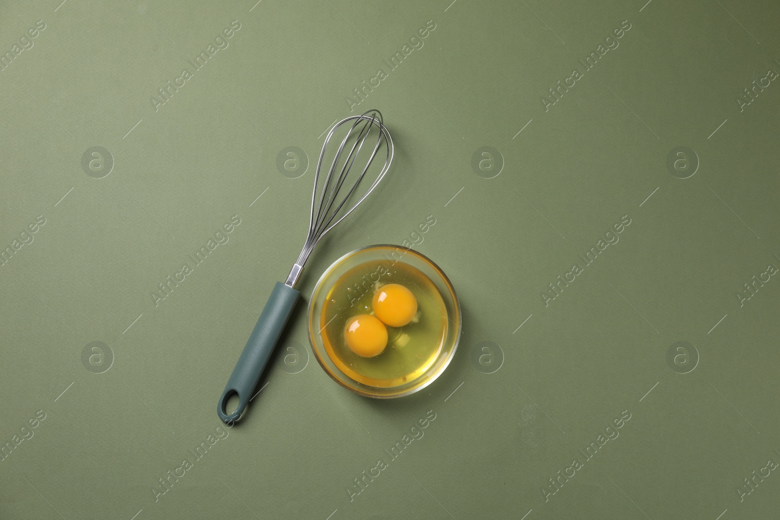 Photo of Metal whisk and raw eggs in bowl on khaki background, flat lay