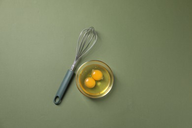 Photo of Metal whisk and raw eggs in bowl on khaki background, flat lay