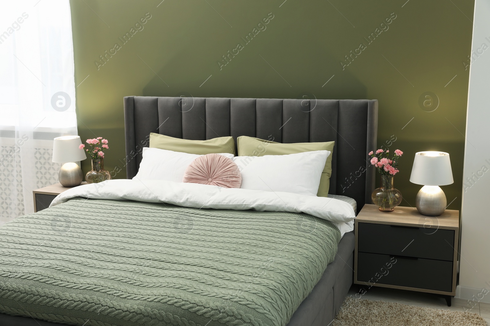 Photo of Large comfortable bed, lamps and beautiful flowers in stylish room. Interior design