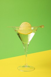 Martini glass of refreshing cocktail with lemon slice on color background