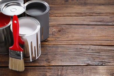 Photo of Cans of paints and brush on wooden table, space for text