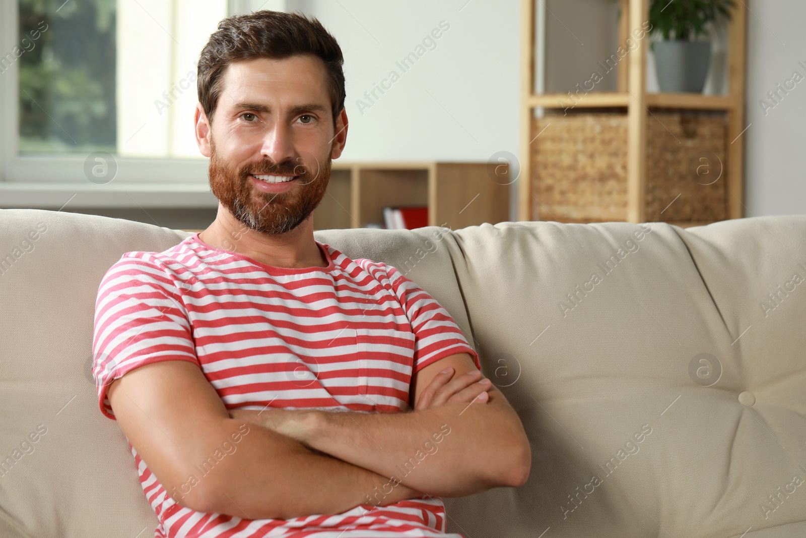 Photo of Portrait of handsome bearded man on sofa at home, space for text