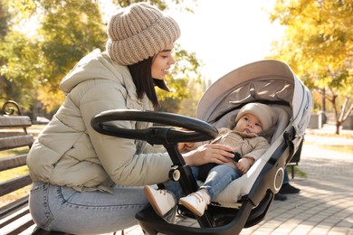 Photo of Happy mother with her baby son in stroller outdoors on autumn day