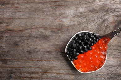 Metal spoon with black and red caviar on wooden background