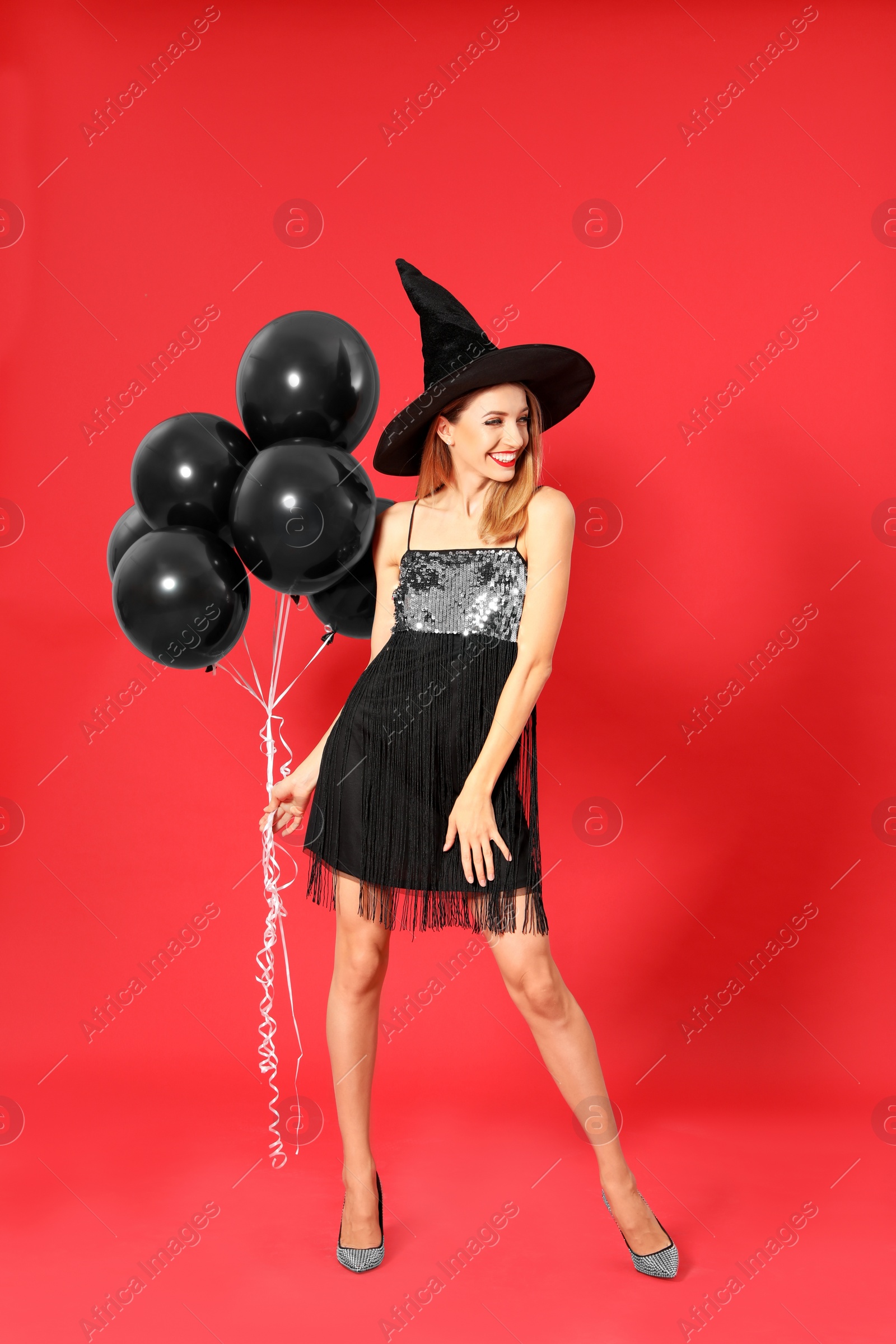 Photo of Beautiful woman wearing witch costume with balloons for Halloween party on red background