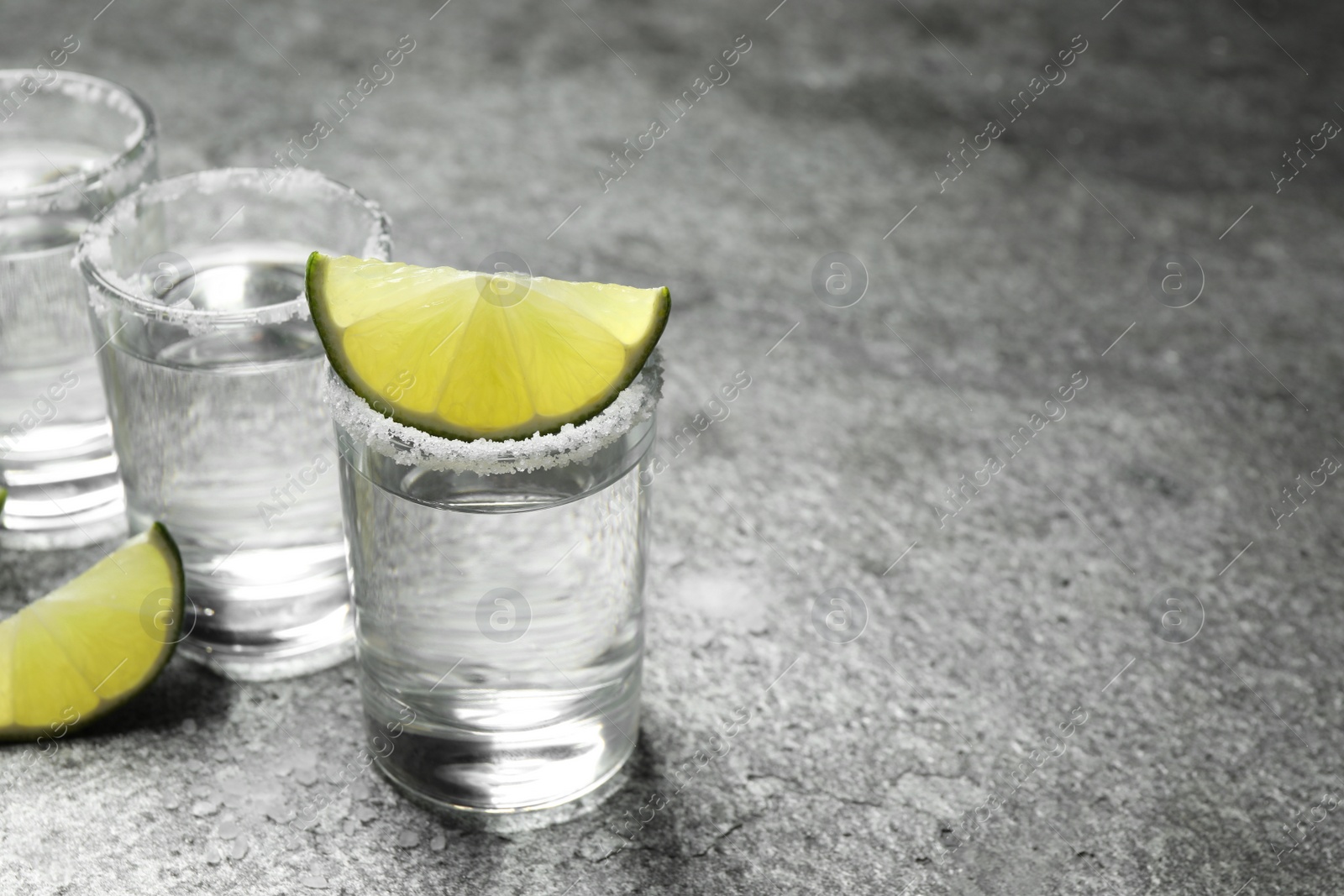 Photo of Mexican Tequila shots with salt and lime slices on grey table. Space for text