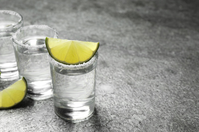 Mexican Tequila shots with salt and lime slices on grey table. Space for text