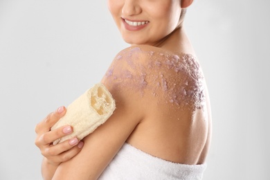 Young woman applying natural scrub on her body against light background