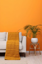 Comfortable sofa with orange blanket and houseplant indoors. Interior design