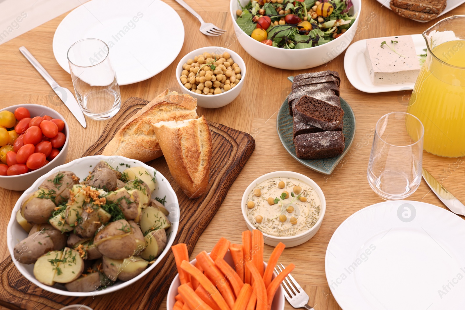 Photo of Healthy vegetarian food, glasses, cutlery, jug of juice and plates on wooden table