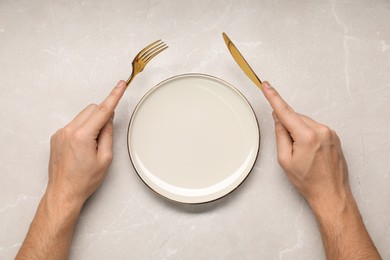Photo of Man holding fork and knife near empty plate at light marble table, top view