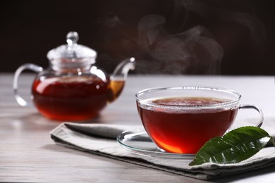 Photo of Aromatic hot tea in glass cup, teapot and leaf on white wooden table. Space for text