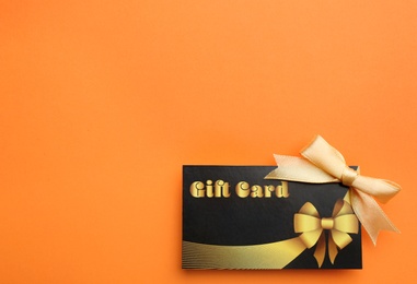 Photo of Gift card with bow on orange background, top view. Space for text