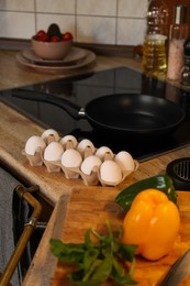 Many fresh eggs in carton and bell pepper on wooden countertop in kitchen. Ingredients for breakfast