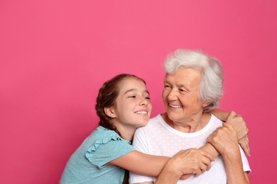 Photo of Cute girl hugging her grandmother on pink background
