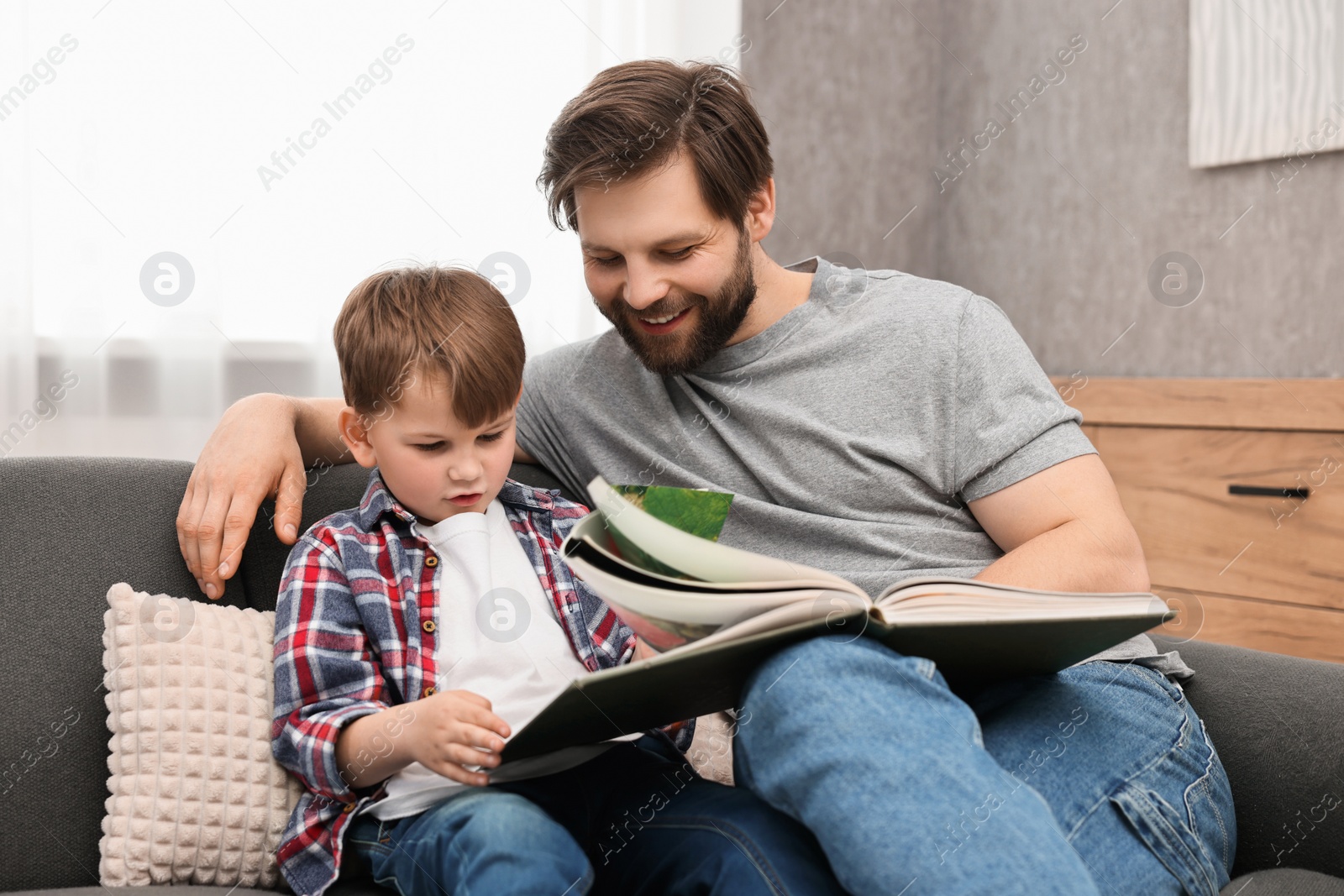 Photo of Dad and son reading book together on sofa at home