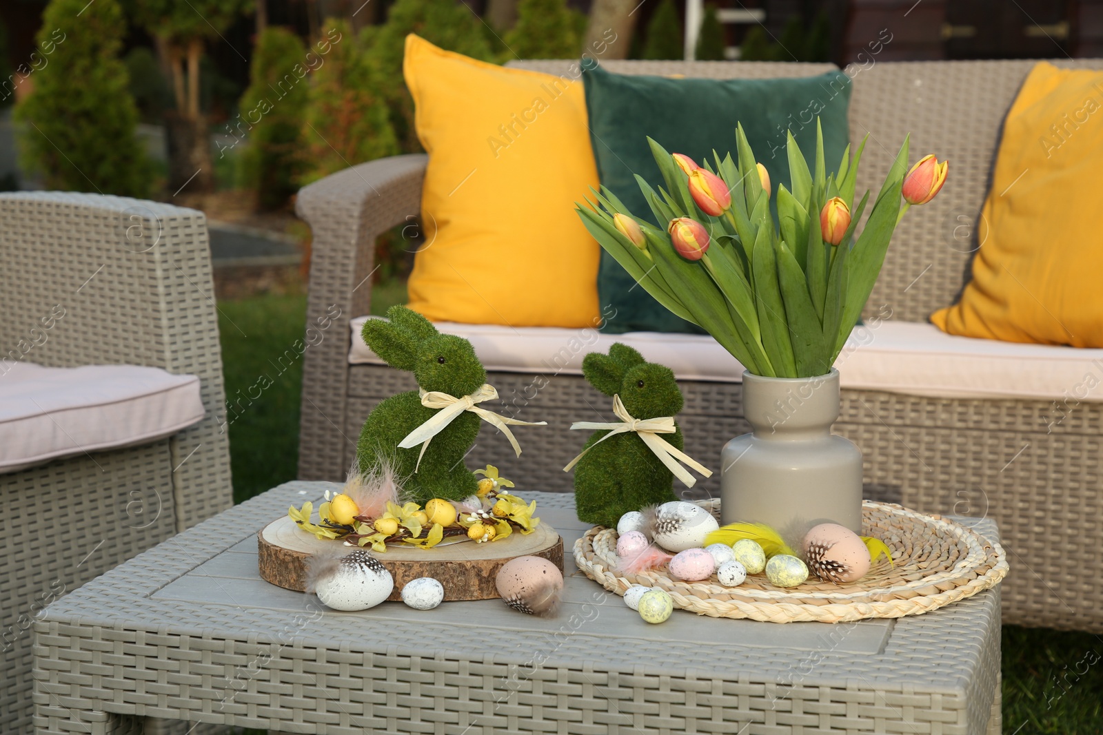 Photo of Terrace with Easter decorations. Bouquet of tulips in vase, bunny figures and decorative eggs on table outdoors