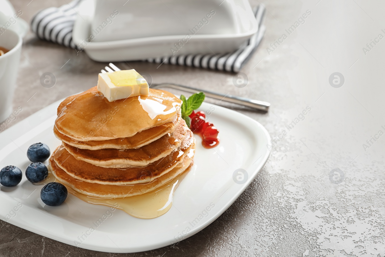 Photo of Stack of tasty pancakes with berries, butter and honey on table