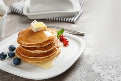 Stack of tasty pancakes with berries, butter and honey on table