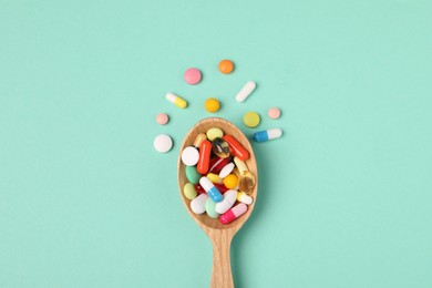 Wooden spoon with many different pills on turquoise background, flat lay