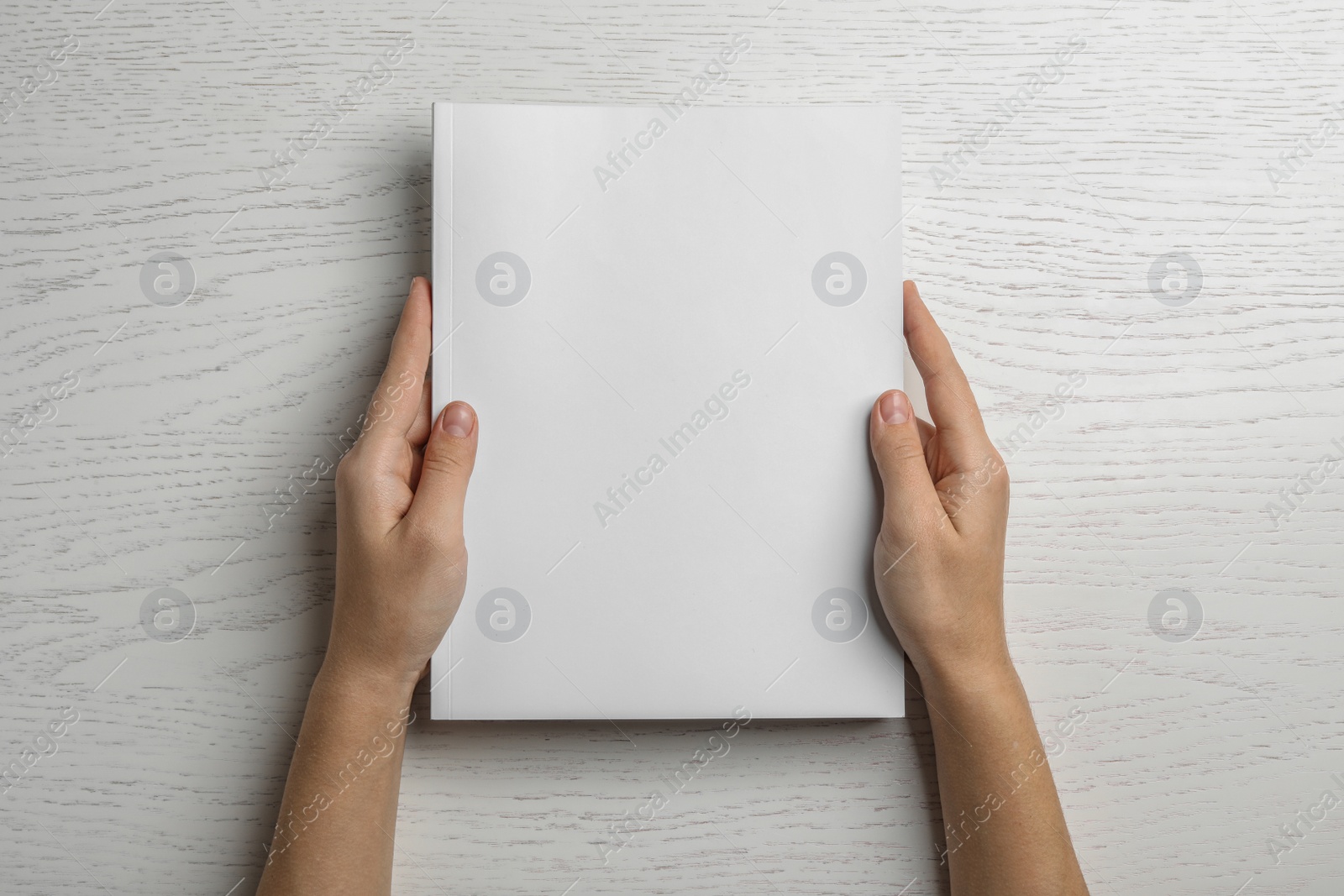 Photo of Woman holding brochure with blank cover on wooden background, top view. Mock up for design