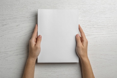 Woman holding brochure with blank cover on wooden background, top view. Mock up for design