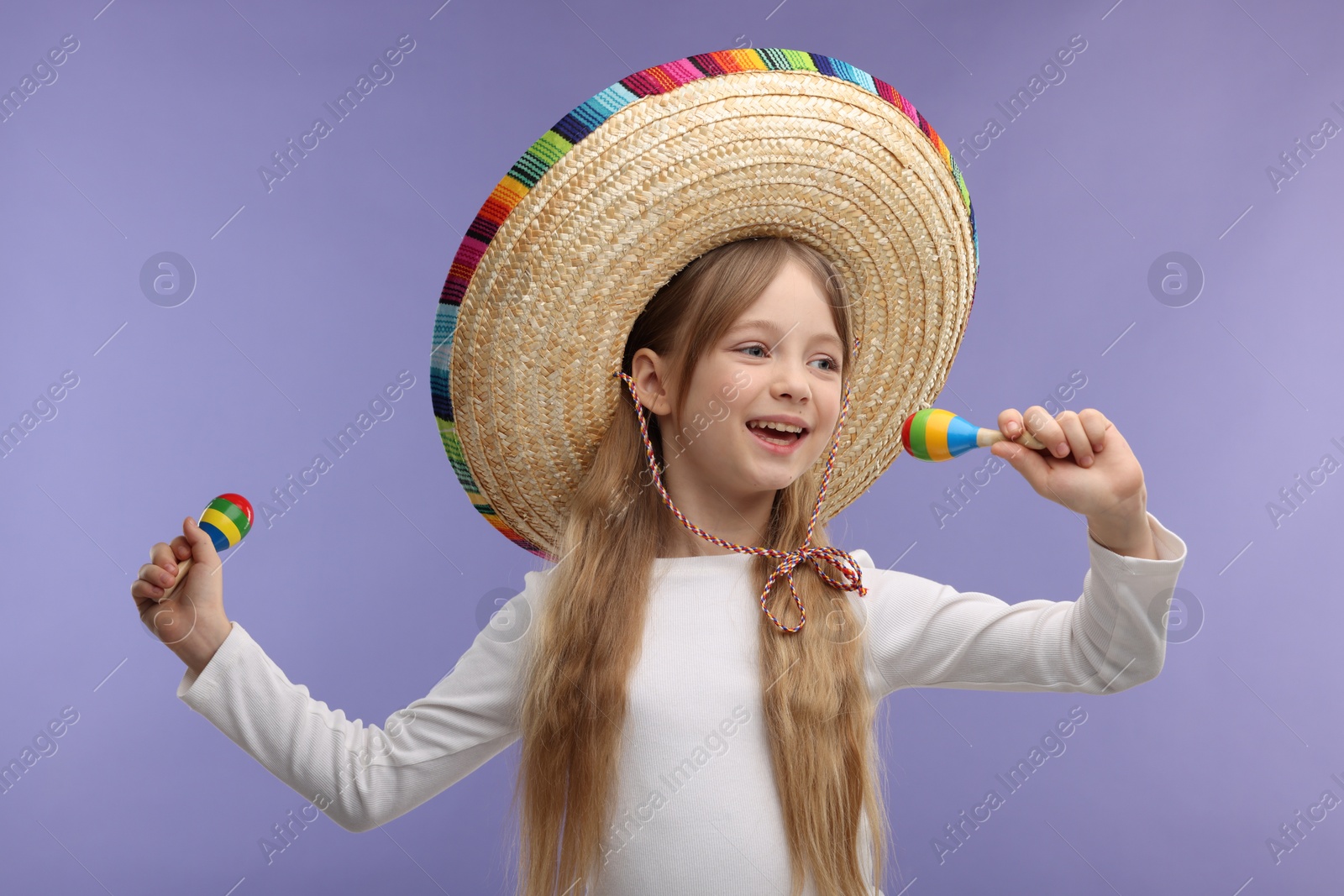 Photo of Cute girl in Mexican sombrero hat singing with maracas on purple background