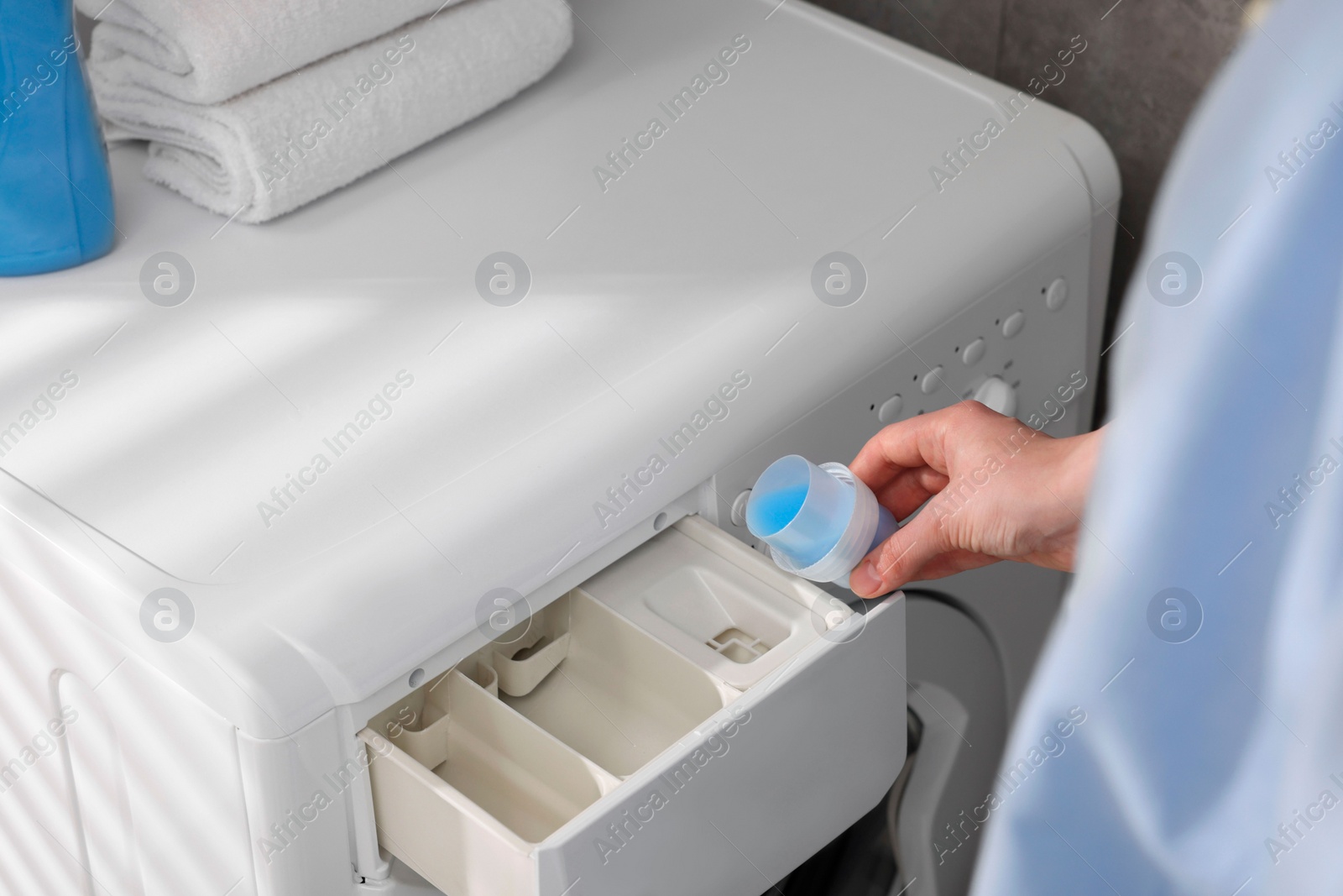 Photo of Woman pouring fabric softener from cap into washing machine, closeup