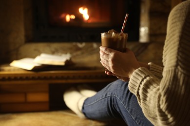 Woman with glass of hot cocoa near fireplace at home, closeup. Space for text