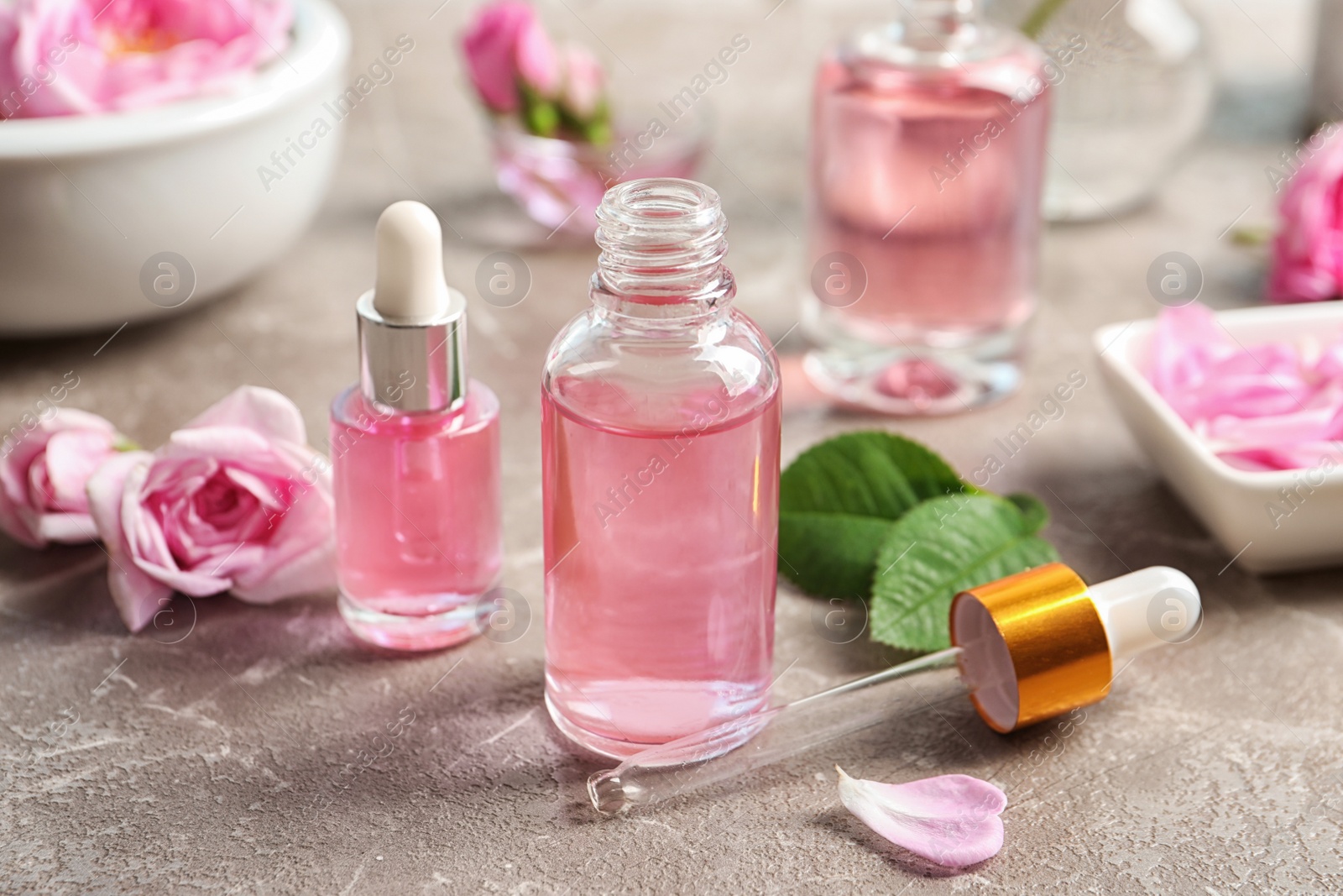 Photo of Bottles of rose essential oil, pipette and flowers on table