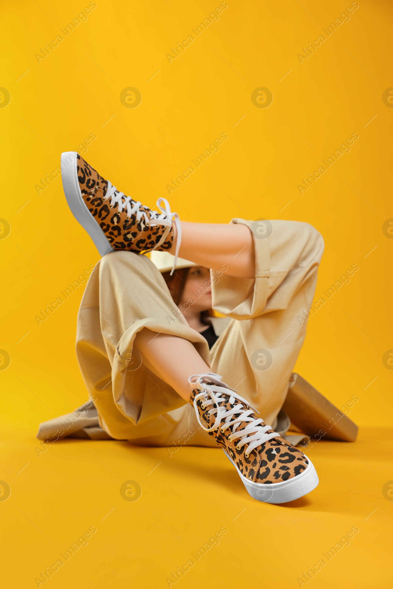 Photo of Stylish woman posing in classic old school sneakers with leopard print on orange background, selective focus