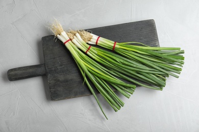 Photo of Black board with bunches of green onions on grey stone table, top view