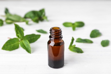 Photo of Bottle of mint essential oil on white wooden table