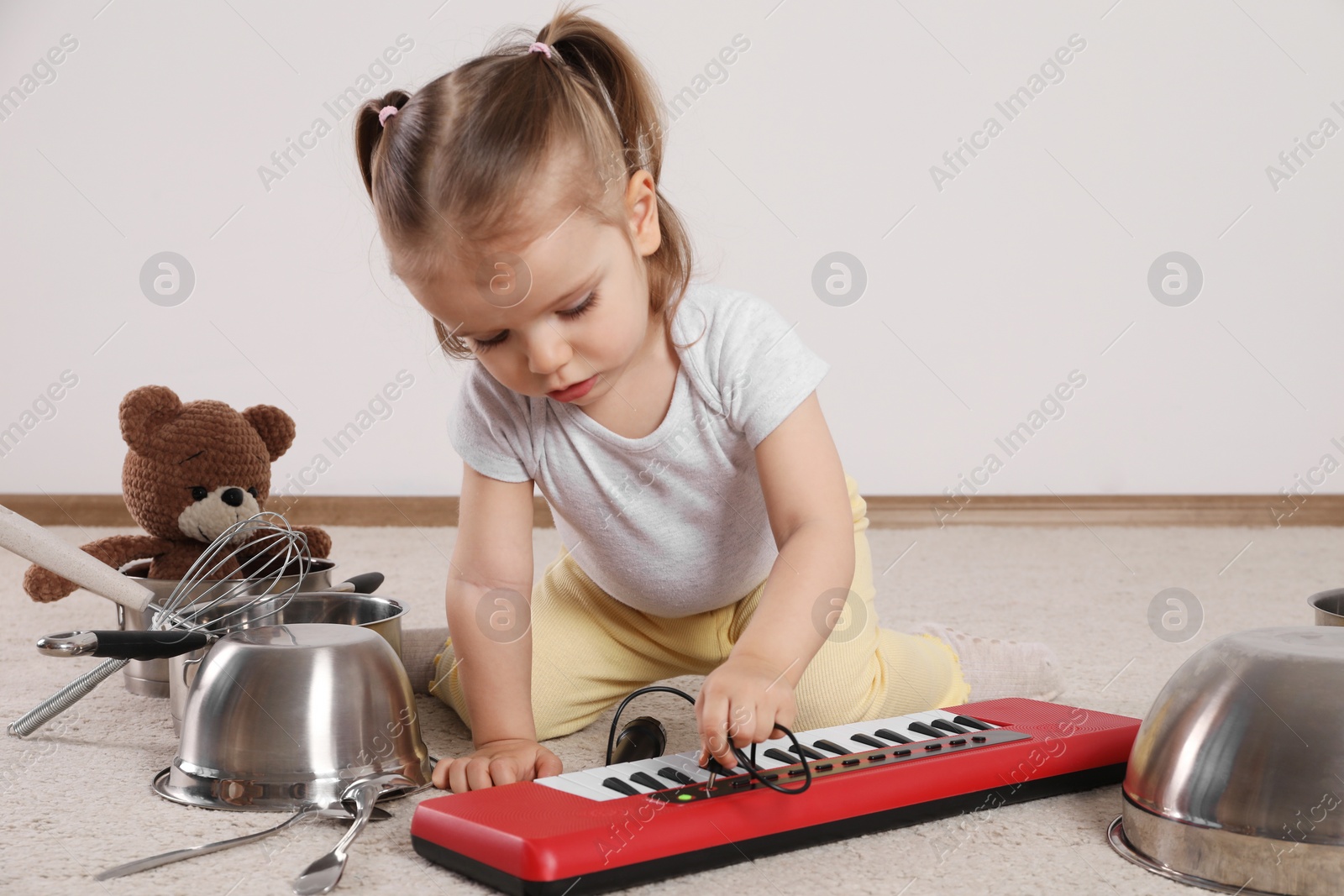 Photo of Cute little girl with cookware and toy piano at home