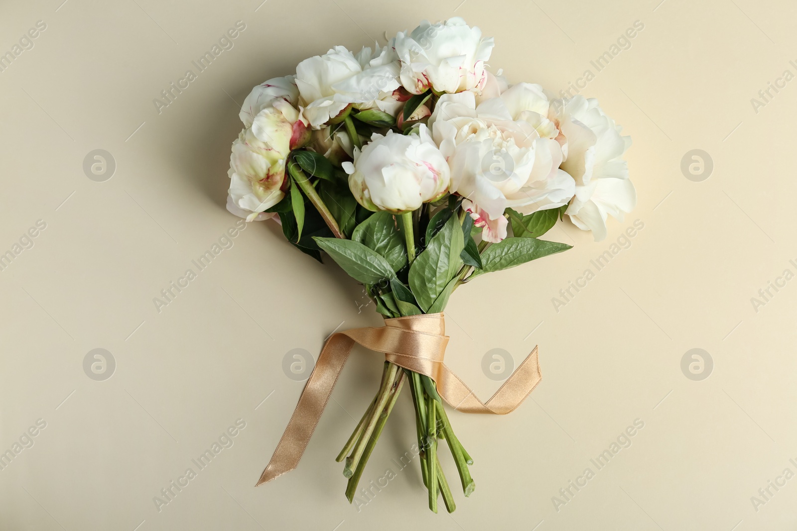 Photo of Bouquet of beautiful peonies with ribbon on beige background, flat lay
