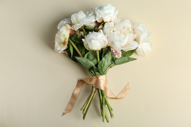 Bouquet of beautiful peonies with ribbon on beige background, flat lay